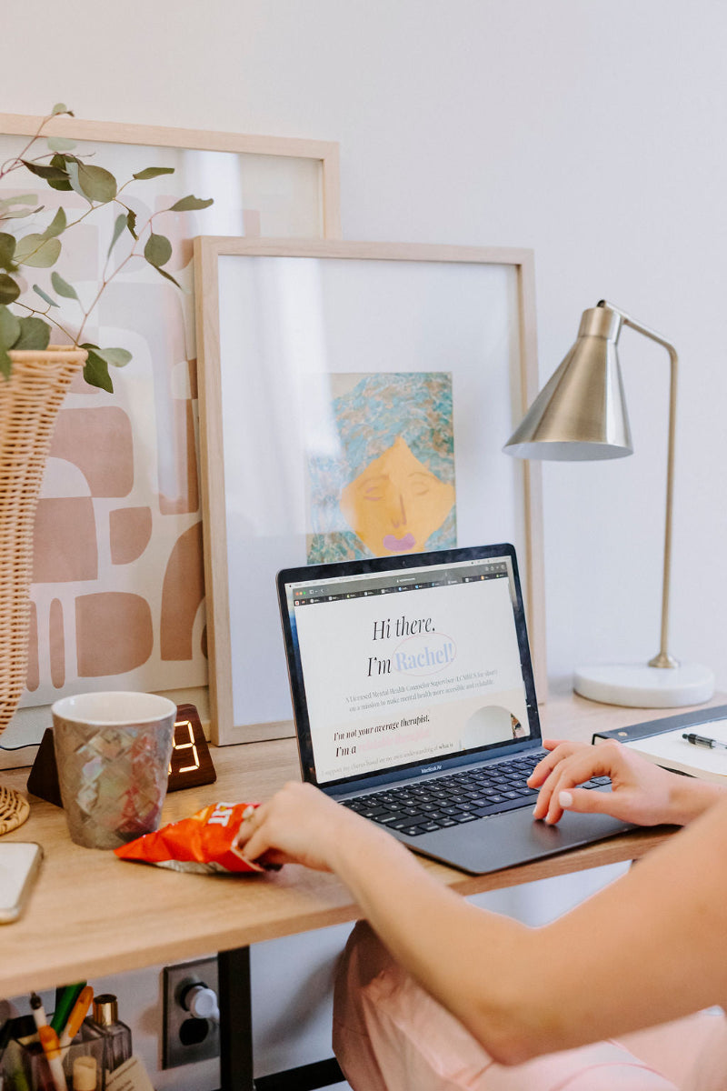 Person using a laptop on a desk with a mug, snacks, and decor items.